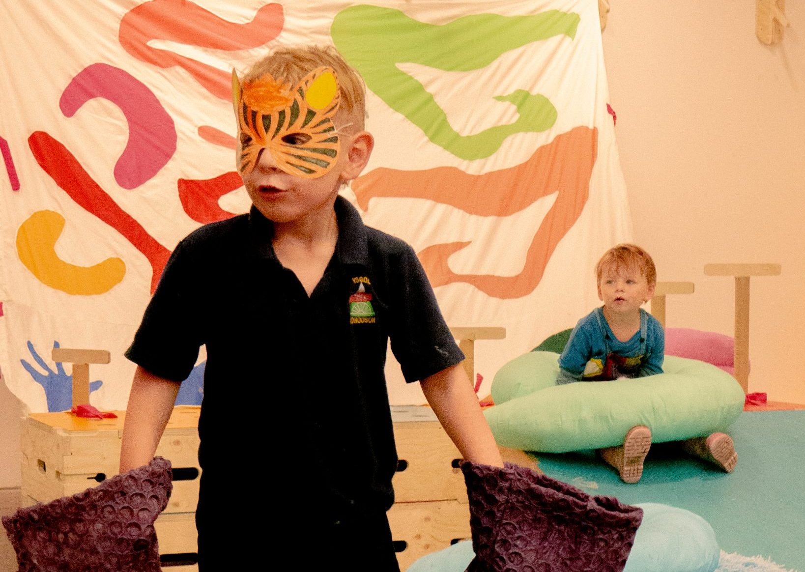 A child wearing a tiger mask, surrounded by colourful soft toys/artworks designed by Ella Jones.