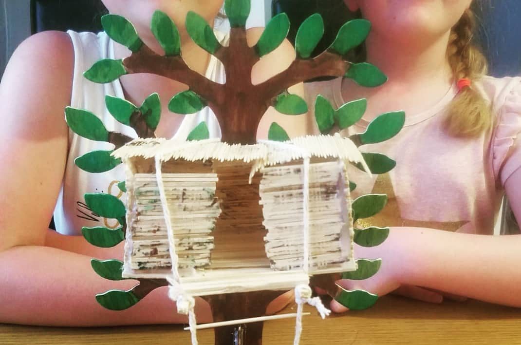 A homemade model of a tree house. Two primary school aged girls can be seen sitting in the background.